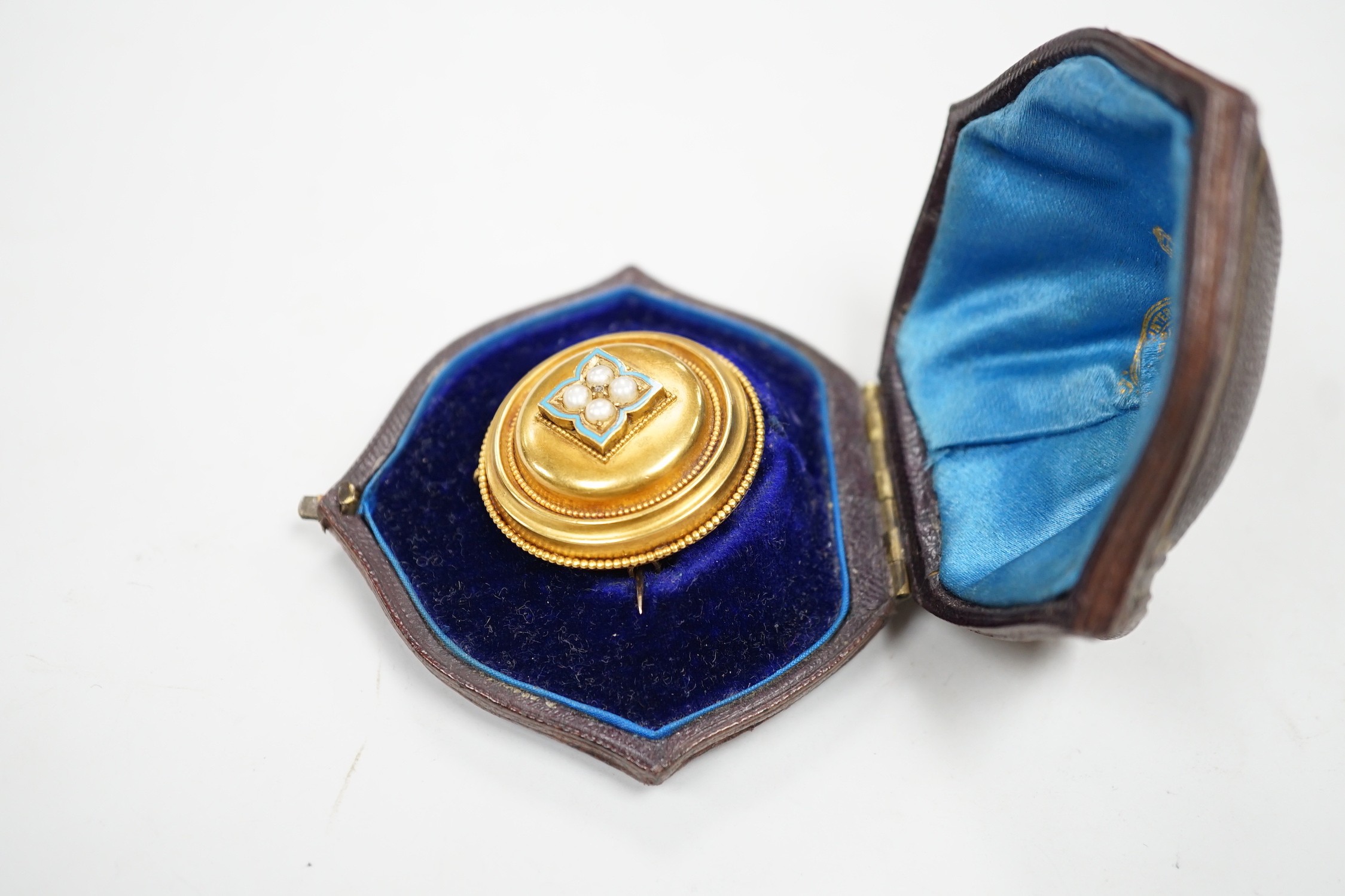 A cased Victorian yellow metal, enamel and split pearl set circular mourning pendant brooch, the glazed back with lock of hair beneath, diameter 34mm, gross weight 12.6 grams.